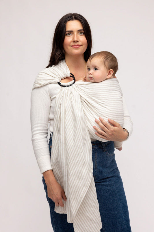 Woman holding a baby in a white woven carrier against a plain background