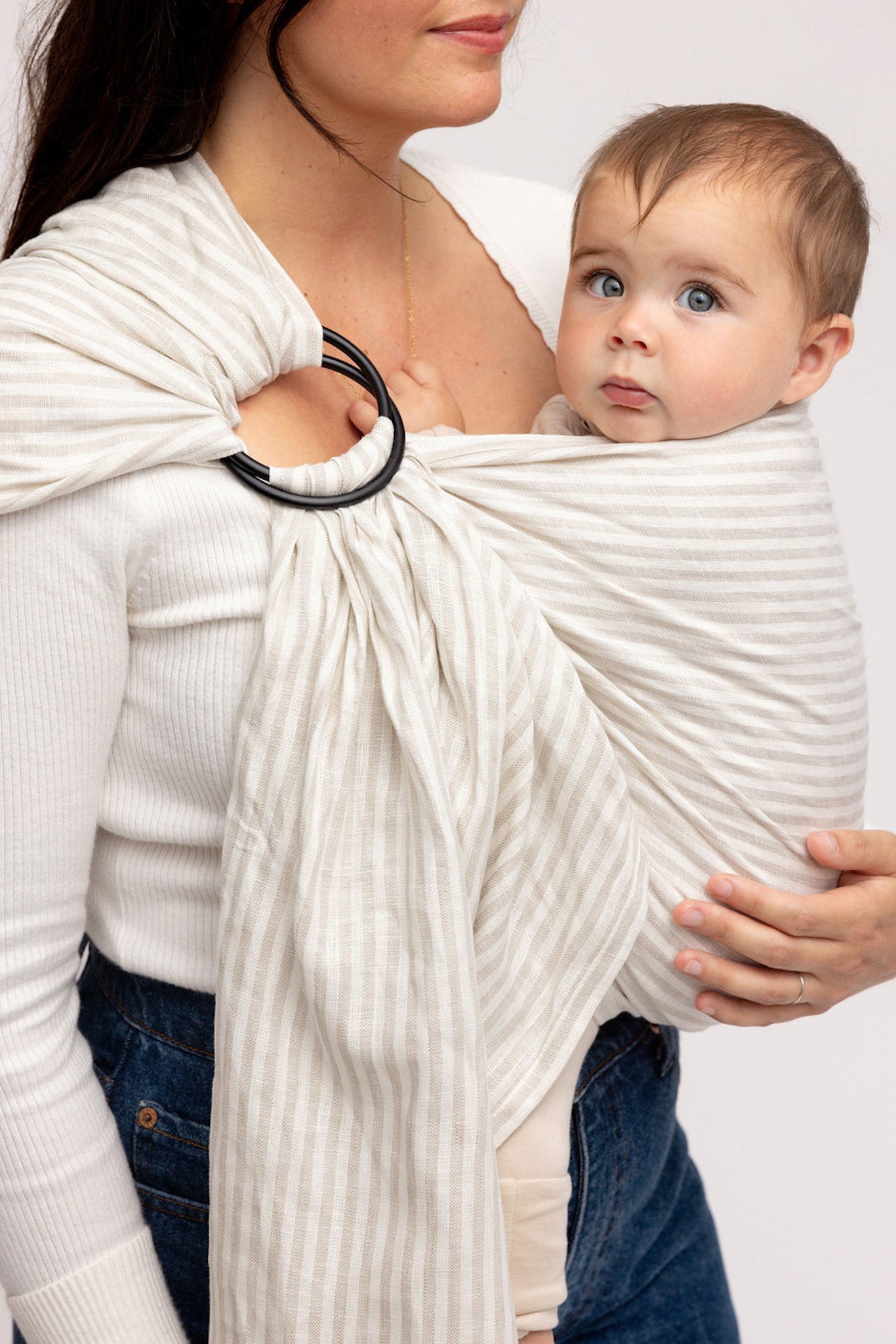 Woman holding a baby in a white sling against a plain background