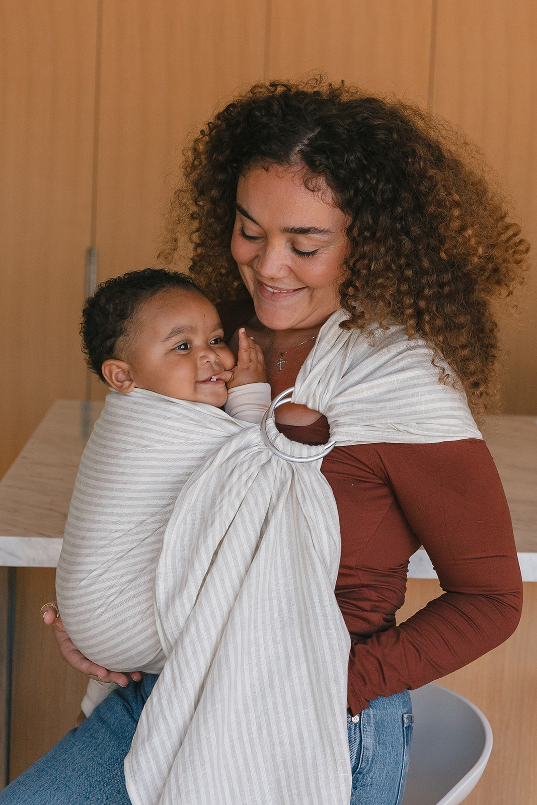 Woman holding a baby wrapped in a white sling against a wooden background