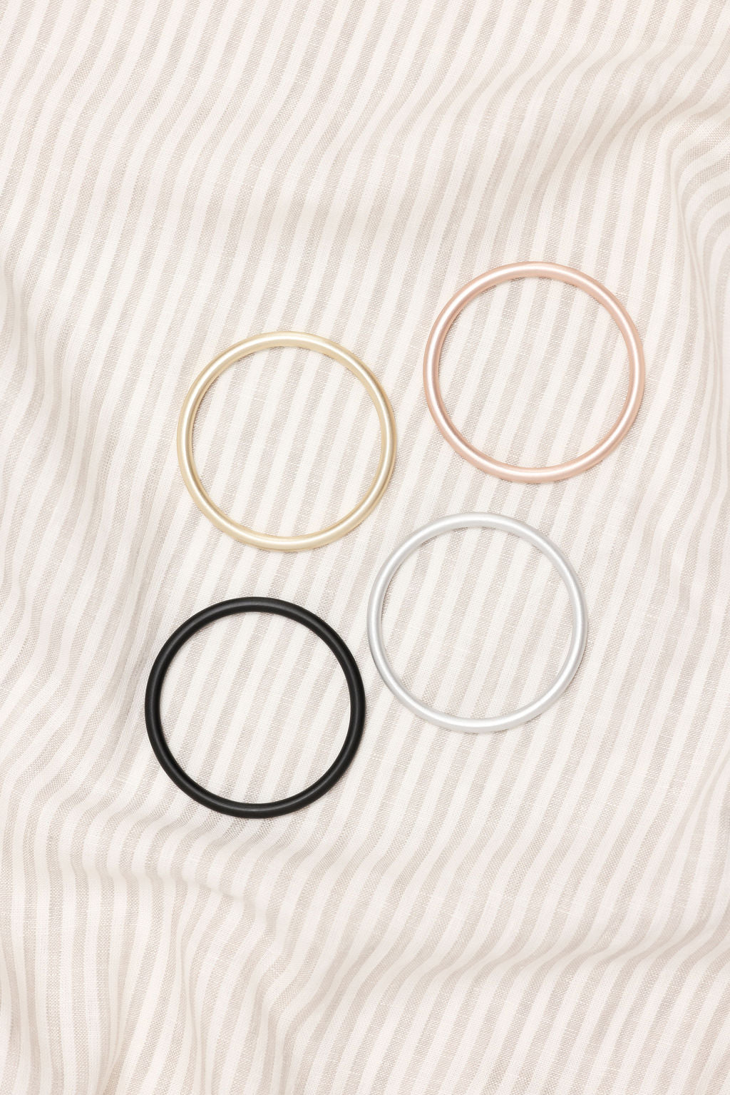 Four metal rings in gold, pink, black, and silver on a striped beige background